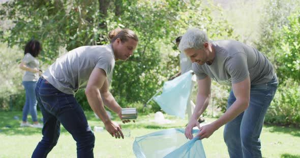 Two caucasian young male volunteers collecting plastic material in a bag and high fiving each other alt