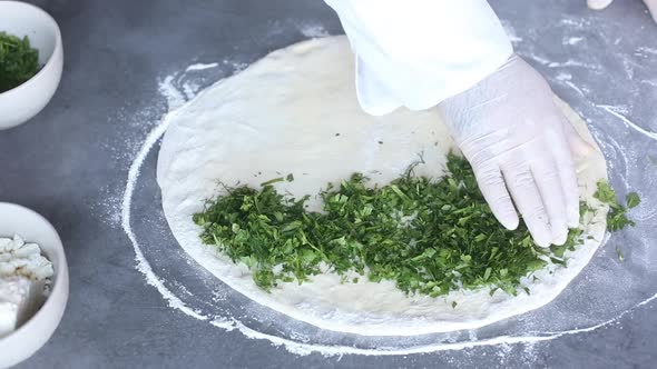 Chef works with dough to prepare national bread with parsley,dill, cilantro and cheese