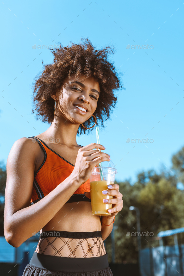 young african-american woman in bright sports bra holding orange juice  Stock Photo by LightFieldStudios