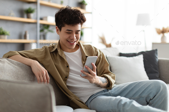 Closeup of smiling asian man using smartphone at home
