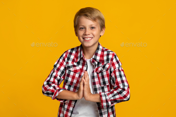 Smiling european adolescent boy modern student holds hands pressed together, prays as good mark