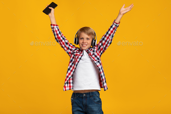 Glad happy emotion excited caucasian teen boy in headphones holding smartphone, jumping, dancing