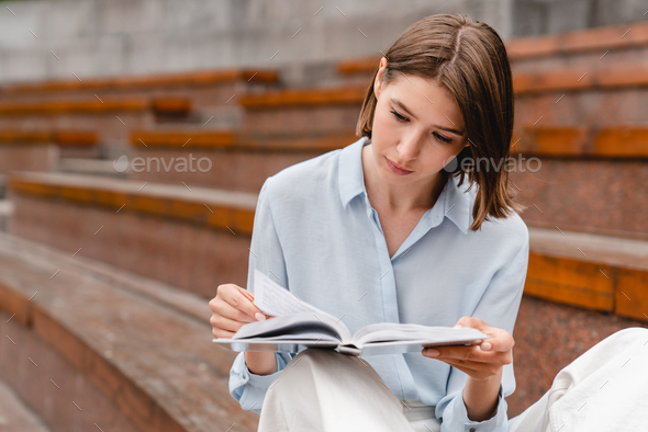 Young student woman freelacer reading book preparing for educational exam at college