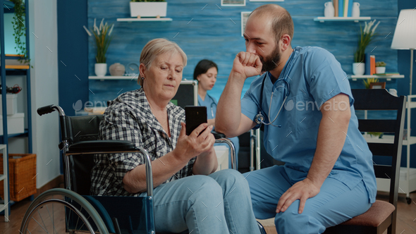 Medical assistant teaching disabled old woman to use smartphone