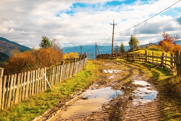 A path along the ridge of a hill with a large puddle and an old fence against the backdrop of a