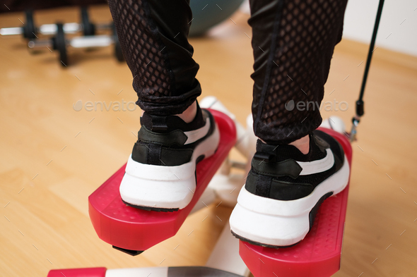 Back view on the woman feet in sneakers doing exercising on the twist stepper or stair stepper