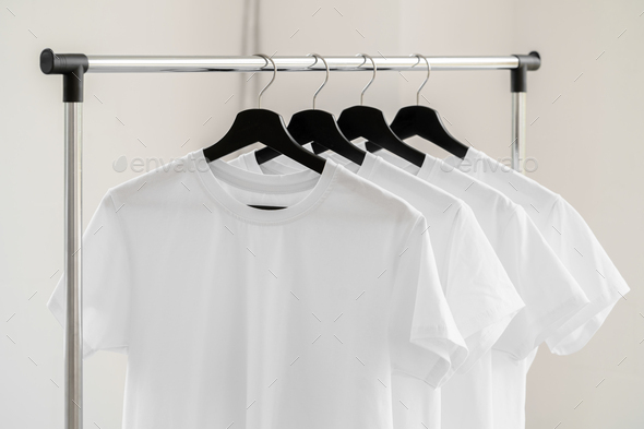 Row of white t-shirts on hangers on rack Stock Photo by FabrikaPhoto