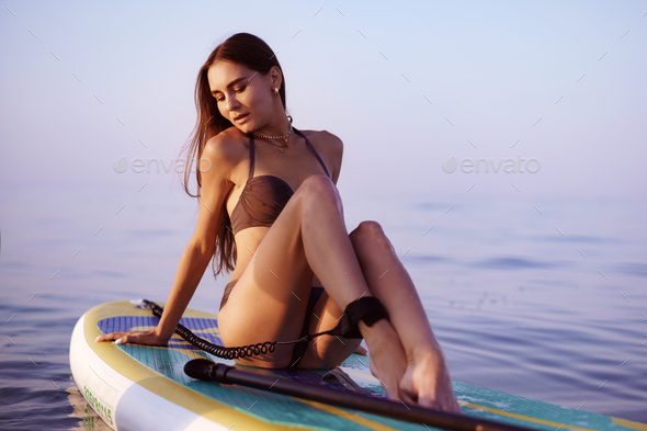 Young woman with sexy fit body posing on paddle board in the sea Stock  Photo by FabrikaPhoto