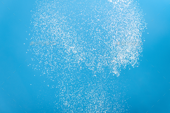 White powder splashes isolated on blue background. Flour sifting on a lue background