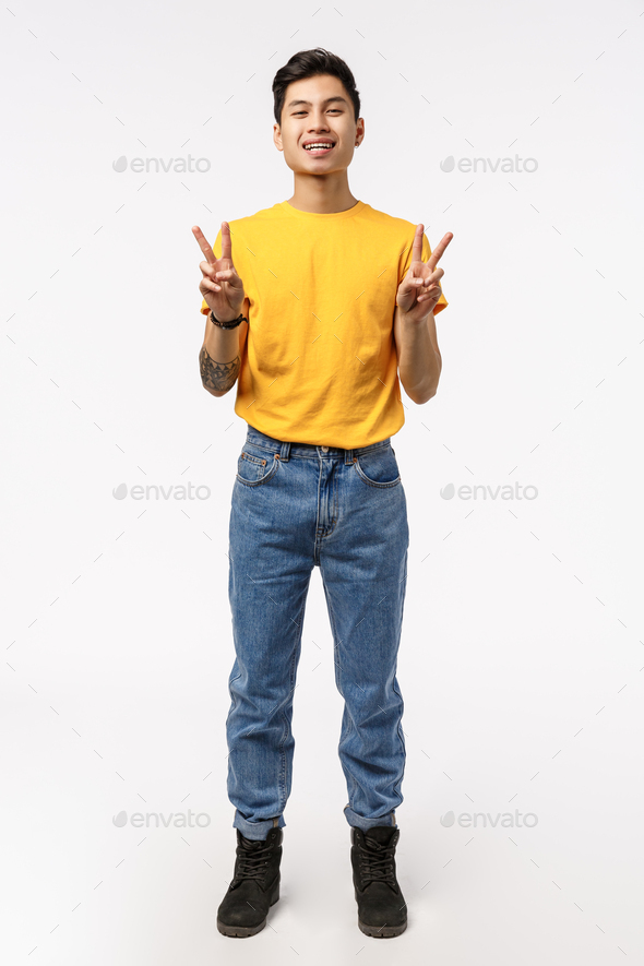 Vertical full-length shot charming chinese guy in yellow t-shirt, jeans, showing peace sign and