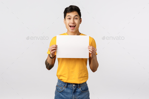 Enthusiastic, thrilled handsome chinese guy with tattoos, holding sign, blank piece paper over chest