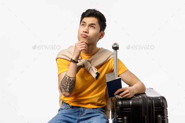 Thoughtful good-looking chinese guy traveller, sitting black suitcase with luggage, touch chin
