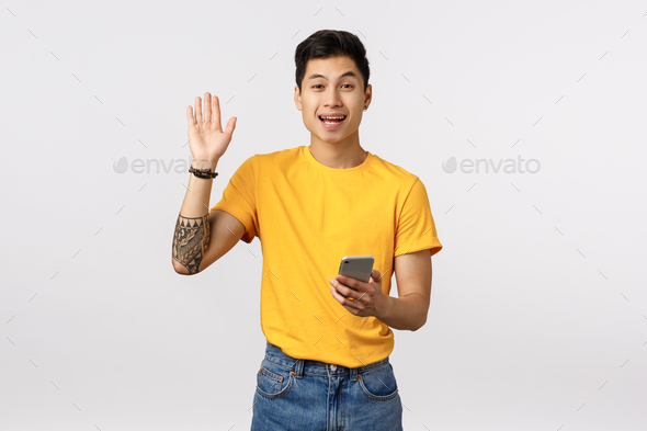 Guy waving raised hand in hello, its me or greeting gesture and friendly smiling, holding smartphone