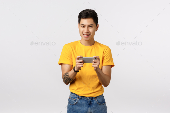 Lets play. Asian guy eager show his gaming skills, holding smartphone horizontally both hands, tap