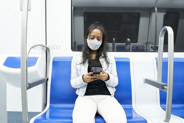Black woman sitting alone in the subway car using a smartphone.