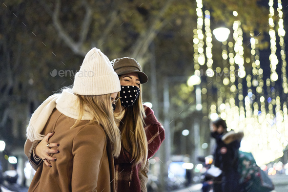 In winter, in the street, at the pedestrian crossing, two young friends wearing masks