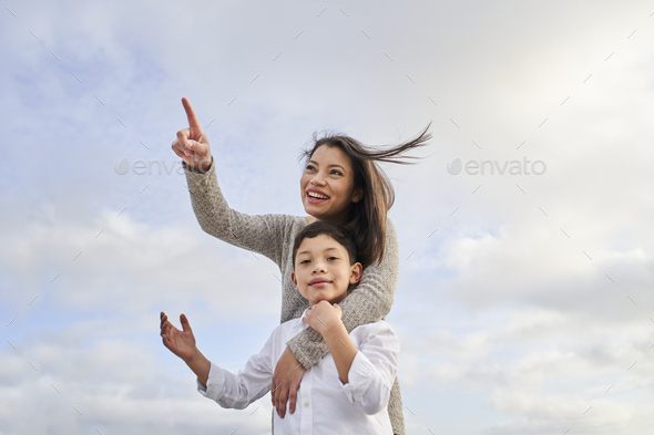 Young Latina mother pointing to some point while her son looks at camera,