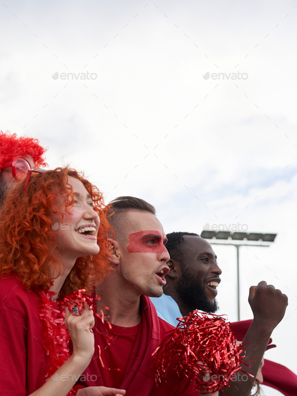 Vertical photo of a group of people of different races follow the soccer match in the parking lot.