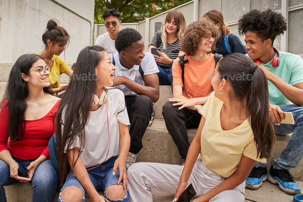Multi-ethnic group of happy students on a break. Young people laugh sitting on the stairs