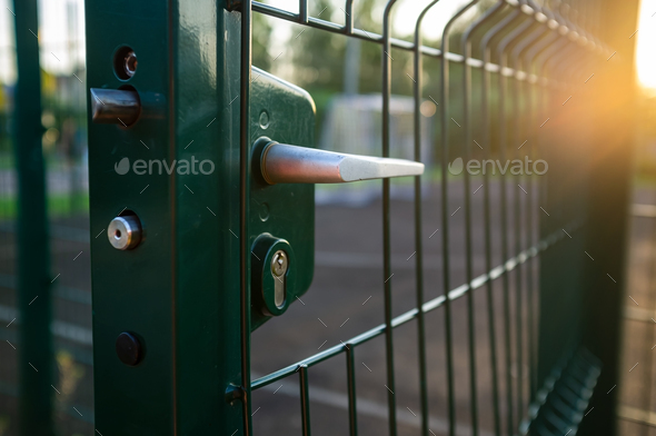Handle with lock on open gate of sports ground fenced with welded mesh fence outdoors at sunset