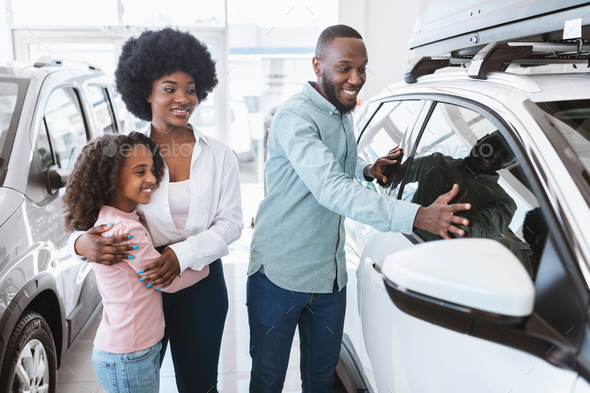 Happy black family selecting new car at auto showroom. Vehicle local distribution concept
