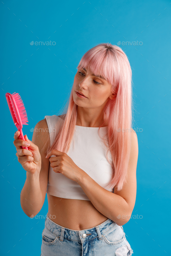 Curious woman with smooth natural long pink hair looking at hair comb