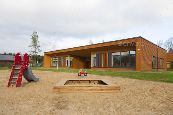 A modern building, nursery or pre-school, a large sand pit play area with a slide.