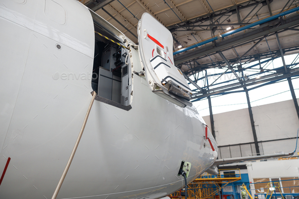 Open aircraft door and cocpit. Passenger airplane on maintenance repair in airport hangar indoors