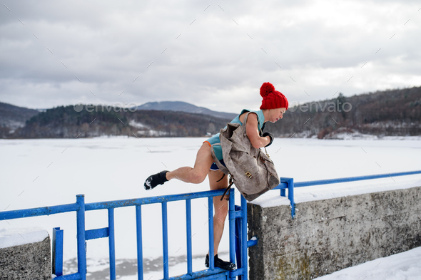 Active senior woman in swimsuit crossing fence outdoors in winter, cold therapy concept