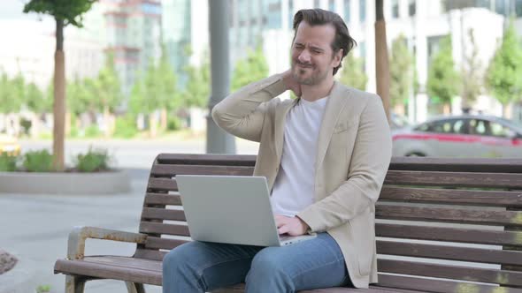 Young Man with Neck Pain Using Laptop While Sitting on Bench alt