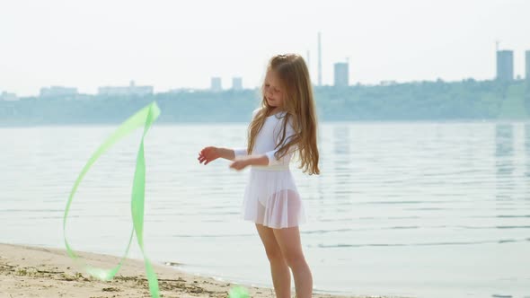 Preschool Girl with Dances a  Gymnastic Ribbon on a Sandy Beach
