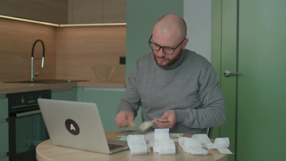 30s Man Counting Dollars for Home Budget with Store Receipts on the Table alt