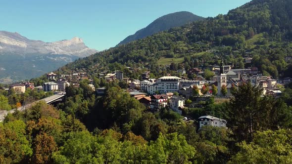 Flying downwards hiding an alpine village behind a tree. St Gervais les Bains, french Alps. Fall col alt