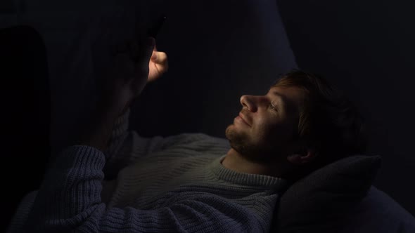 A Man Lying in Bed Uses a Smartphone