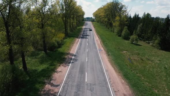 The Drone Flies Over the Road Between the Trees and Watching the Cars