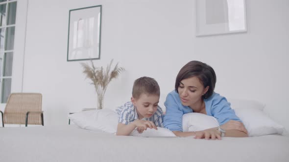 Mother and Son Using Digital Tablet in Bedroom at Home alt