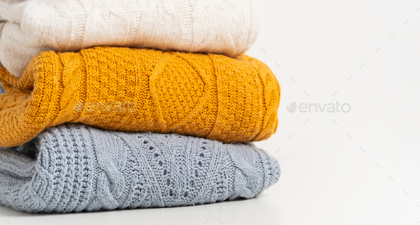 A stack of cozy knitted autumn-winter sweaters in yellow, white, blue colors. Cleaning clothes