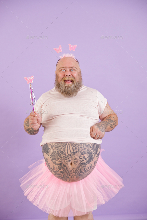 Funny plus size man in fairy costume holds magic stick on purple background