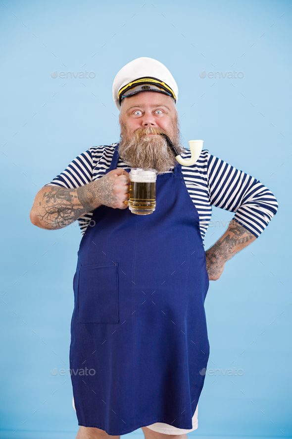 Positive fat man in sailor suit with apron holds craft beer on light ...