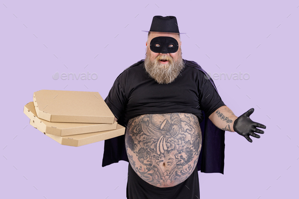 Positive fat man in Zorro costume holds cardboard boxes of pizza on purple background