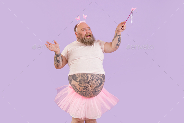 Expressive man with overweight in fairy suit waves magic stick on purple background