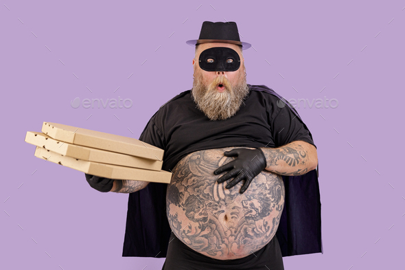 Surprised plump person in Zorro suit holds boxes of pizza on purple background