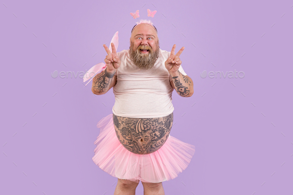 Excited man with overweight in fairy suit shows peace gestures on purple background