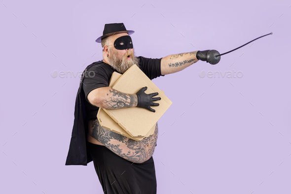 Bellicose fat man in Zorro costume with boxes of pizza stands on purple background