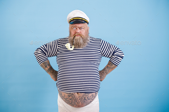 Funny bearded fat man in sailor suit with smoking pipe on light blue ...