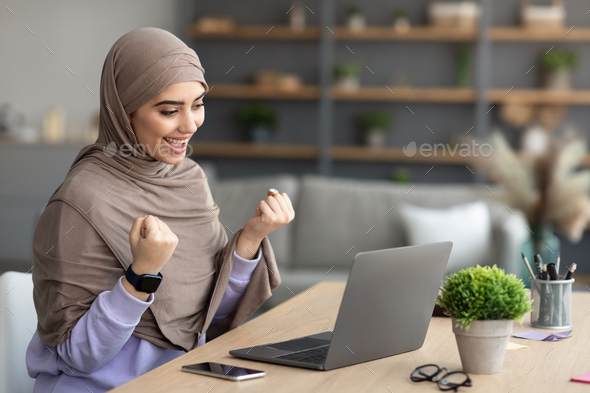 Muslim woman using pc celebrating success shaking fists