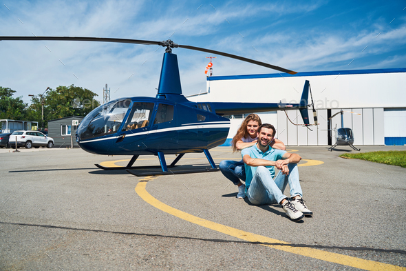 Pleased young Caucasian couple seated on helipad