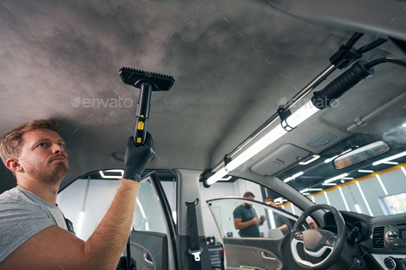 Portrait of worker use car interior steam cleaner. Vapor sterilization  Stock Photo by svitlanah