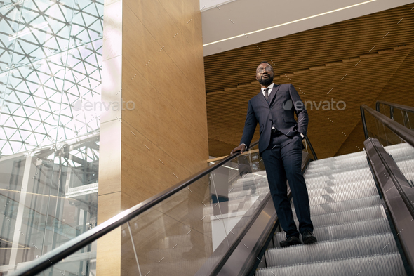 African businessman standing on step of moving escalator