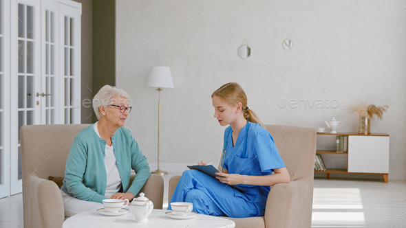 Senior woman with short haircut talks to young female doctor writing notes on clipboard - Stock Photo - Images